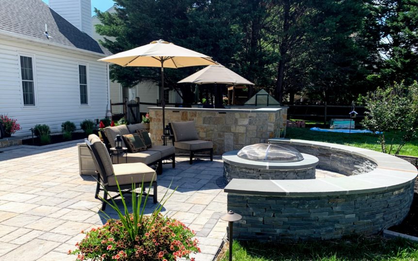 Outdoor living area featuring a paver patio with natural stone grill island and fire pit